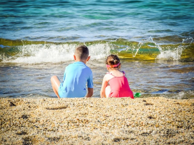 Dos niños sentados en la orilla de la playa mientras rompe una ola